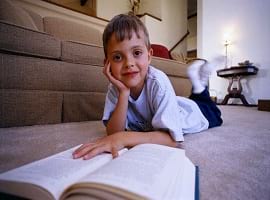 Boy Reading Book on Living Room Floor
